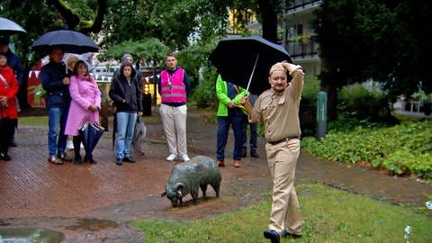 Der Hauptdarsteller Bobby steht mit Regenschirm vor einigen Zuschauern. Bei der Premiere von "Rendezvous durch die Zeiten" hat es lange geregnet. Das Stück ist ein Mix aus Musical, Theater und Stadtführung. 