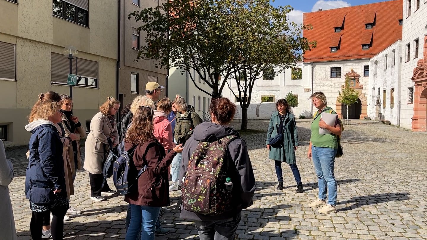 Eine Gruppe aus Lehrerinnen und Lehrern hört den beiden Stadtführerinnen zu. Sie stehen vor dem Zeughaus in Ulm.