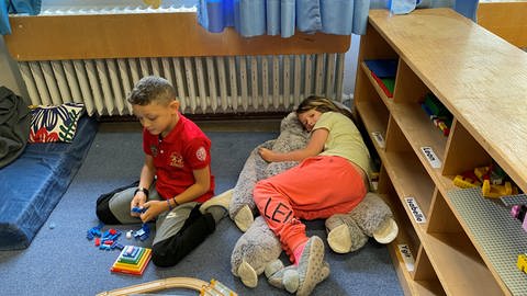 Ein Junge baut Lego in einer Spielecke in der Hans-Zulliger-Schule in Ulm. Ein Mädchen liegt auf ihrem riesigen Kuscheltier und ruht sich aus. Die beiden Kinder sind gerne in der Hans-Zulliger-Schule.