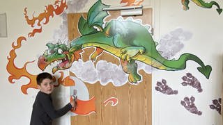 Auf der Eingangstür des "Drachenzimmers" ist ein feuerspeiender Drache abgebildet. Ein Junge will die Türe gerade öffnen. In diesem Zimmer können sich Kinder austoben, bis die starken Gefühle nachlassen.