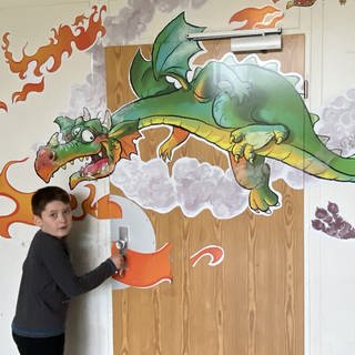 Auf der Eingangstür des "Drachenzimmers" ist ein feuerspeiender Drache abgebildet. Ein Junge will die Türe gerade öffnen. In diesem Zimmer können sich Kinder austoben, bis die starken Gefühle nachlassen.