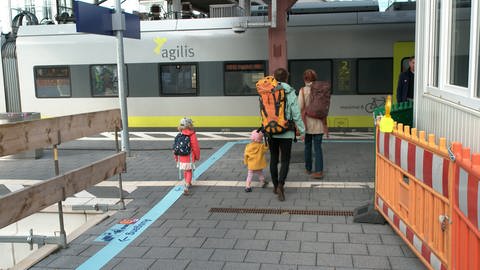 Eine Familie läuft zwischen zwei Absperrungen Richtung Gleise. Der Durchgang ist circa 2,5 Meter Breit. In Ulm bleibt die Bahnhofshalle wegen eines Umbaus zwei Jahre lang geschlossen.