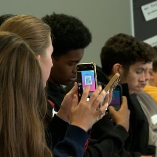 Schülerinnen und Schüler zücken beim Newscamp von SWR und SWP in Ulm ihr Handy bei einem interaktiven Workshop zum Thema Influencer und Desinformation.