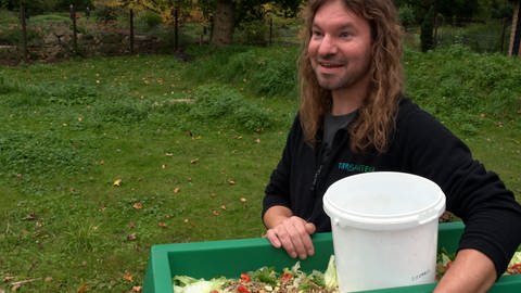 Andreas Gerstenberger vom Tiergarten Ulm hält lächelnd einen Kübel voller Tierfutter für die Kängurus unter dem Arm