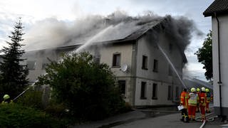 Feuerwehrleute löschen ein Gebäude, aus dem viel Qualm dringt: Großbrand in Amstetten im Alb-Donau-Kreis: Damit die Feuerwehr die Flammen im Gebäudeinnern löschen konnte, musste sie die Scheiben einwerfen. Nach den Löscharbeiten wurde im Gebäude ein toter Mann gefunden.