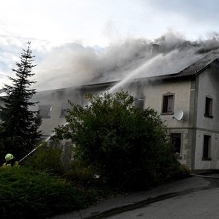 Feuerwehrleute löschen ein Gebäude, aus dem viel Qualm dringt: Großbrand in Amstetten im Alb-Donau-Kreis: Damit die Feuerwehr die Flammen im Gebäudeinnern löschen konnte, musste sie die Scheiben einwerfen. Nach den Löscharbeiten wurde im Gebäude ein toter Mann gefunden.