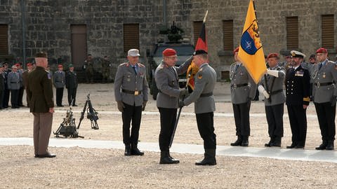 Generalleutnant Kai Ronald Rohrschneider nimmt bei einer Zeremonie im Innenhof der Ulmer Wilhelmsburg, die Fahne des Multinationalen Kommandos Operationale Führung entgegen. Sie wird ihm gereicht vom Generalinspekteur der Bundeswehr, Carsten Breuer, der sie von Generalleutnant Alexander Sollfrank bekommen hatte.