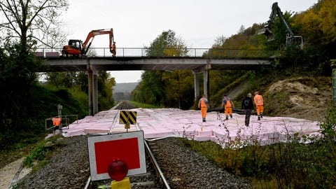 Bagger auf einer Brücke, Schutz für Gleise durch Styropormatten: Der Abriss einer maroden Brücke bei Blaustein hat schon am Samstag begonnen. So kann die Bahnstrecke Ulm-Blaubeuren womöglich früher wieder freigegeben werden. 