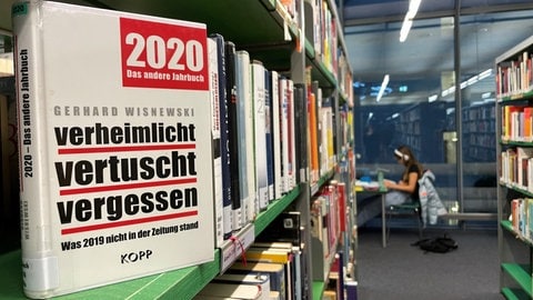 Ein Bücherregal in der Ulmer Stadtbibliothek. Im Bereich Geschichte stehen hunderte Bücher - ihre Ansichten so bunt gemischt wie die Farben ihrer Einbände. Im Hintergrund arbeitet jemand an einem Tisch.