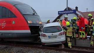 Zug und Auto nach einem Zusammenstoß, Rettungskräfte darum herum: Vom Zug erfasst, halb auf dem Bahnsteig: Ein 18-jähriger Autofahrer ist am Donnerstagmorgen bei Aletshausen im Kreis Günzburg mit einer Regionalbahn zusammengestoßen.