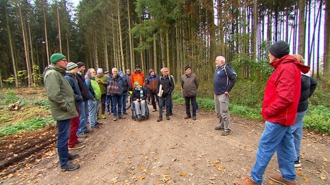 Etwa zwanzig Personen stehen im Wald bei Ulm-Jungingen. Ein Sprecher des Ulmer Klimanetzes erläutert, wo Windräder für einen geplanten Windpark gebaut werden könnten. 