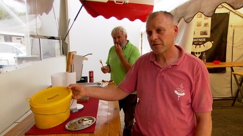 Ein Mann an einem Tisch, darauf ein gelber Eimer: Seit acht Jahren betreibt Peter Hafner seinen Imbiss im Ulmer Donautal. Eine Registrierkasse hatte er noch nie. Ein Farbeimer geht auch. 