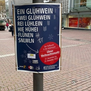 Was steht im Mittelpunkt des Weihnachtsmarktes? Das Plakat gibt eine heitere wie ehrliche Antwort.