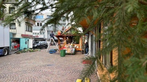 Blick auf eine Bude des Aalener Weihnachtsmarktes, die gerade aufgebaut wird. Im Vordergrund unscharf eine Tanne. Der Weihnachtsmarkt in der Innenstadt ist nur ein paar Gehminuten von dem Eispark entfernt.