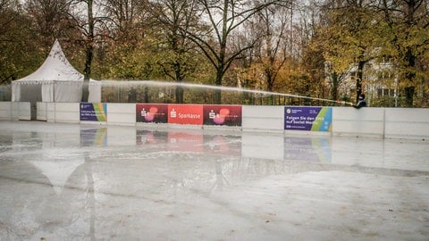 Ein Mitarbeiter des Eisparks auf dem Bohlschulplatz in Aalen spritzt mit einem großen Schlauch Wasser auf die Eisfläche.