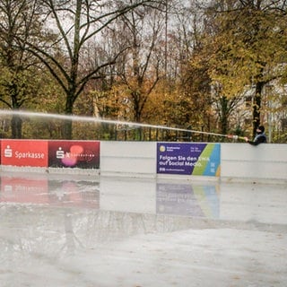 Ein Mitarbeiter des Eisparks auf dem Bohlschulplatz in Aalen spritzt mit einem großen Schlauch Wasser auf die Eisfläche.