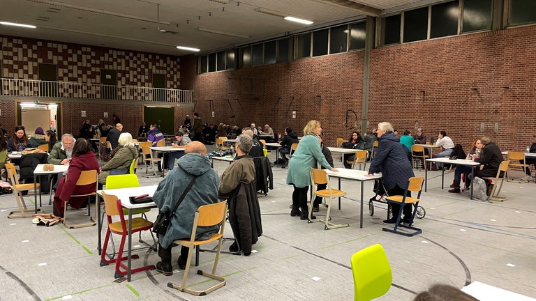 Die evakuierten Menschen sitzen an Tischen in der Sporthalle des Kepler-Gymnasiums in Ulm. Sie mussten ihre Wohnungen wegen dem Fund einer Fliegerbombe verlassen.