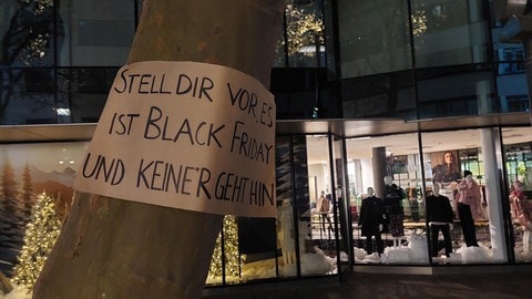 Ein Plakat an einem Baum in der Ulmer Innenstadt, dahinter ein weihnachtlich geschmücktes und beleuchtetes Schaufenster. Das trägt eine klare Botschaft: Protest gegen Konsum und Schnäppchenjagd am Black Friday. Die letzte Generation hat in der Nacht zum Samstag ind er Ulmer Innenstadt Banner und Plakate aufgehängt mit Mahnungen und dem Aufruf, zugunsten der Umwelt auf Billigware zu verzichten. (29.11.)