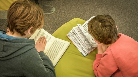 Zwei Jungs, die in der Ulmer Stadtbibliothek Bücher lesen. Darf es ein Sachbuch, Roman oder oder doch lieber ein lustiger Comic sein? Auf der Kinderbuchmesse in der Stadtbibliothek Ulm findet jedes Kind mit Sicherheit etwas schönes zu lesen.