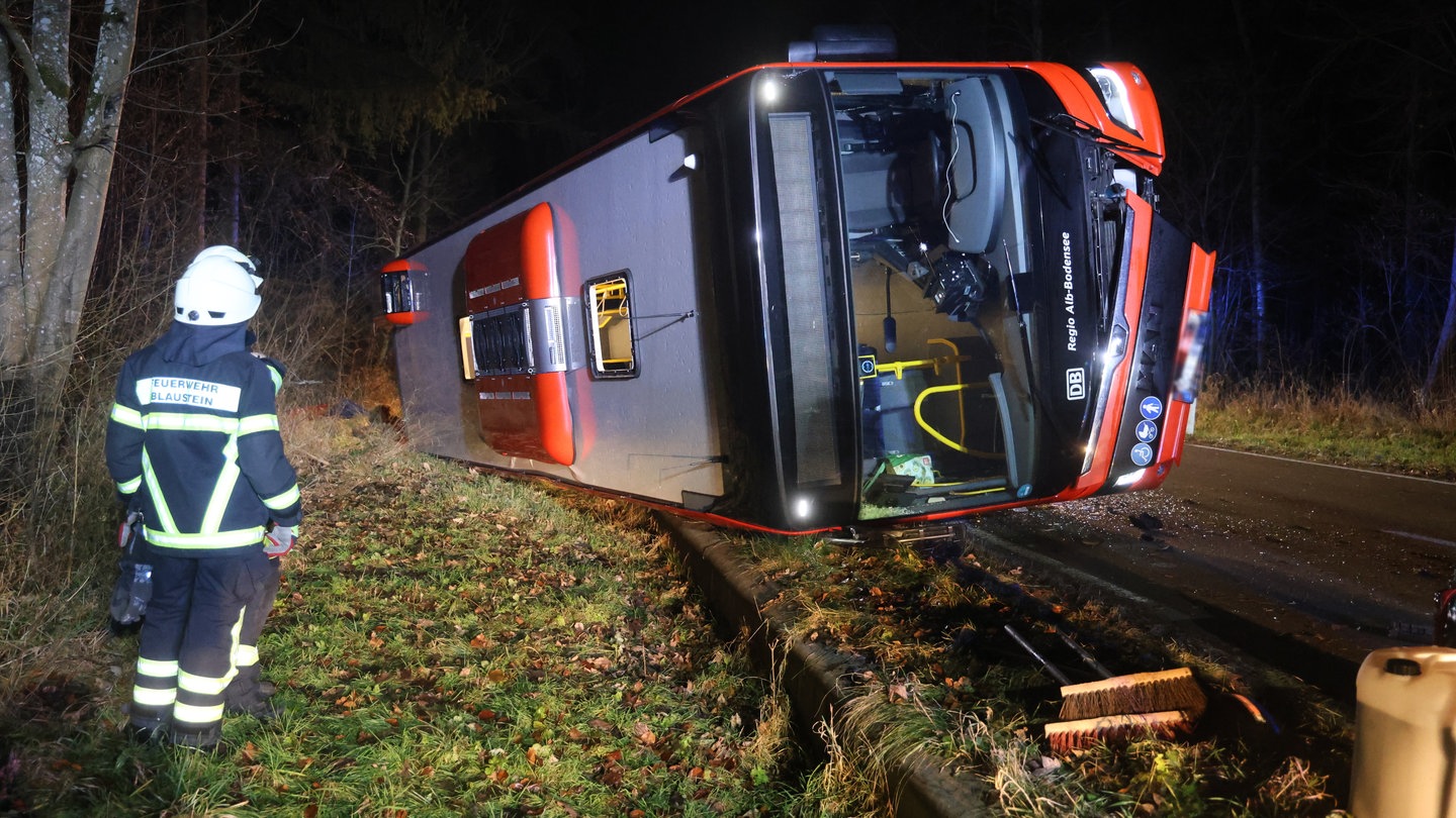 Der umgekippte Linienbus liegt auf der Straße zwischen Blaubeuren und Blaustein. Davor steht ein Feuerwehrmann.