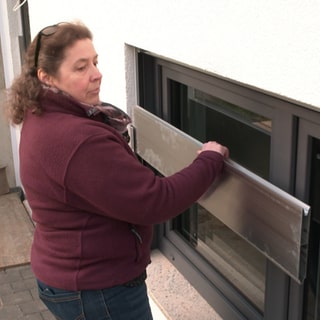 Ursula Weitmann steht mit einem Steckelement vor ihrem Kellerfenster und zeigt wie man es einsetzt. Für das nächste Mal will die Familie aus Illerkirchberg besser gegen Hochwasser geschützt sein.