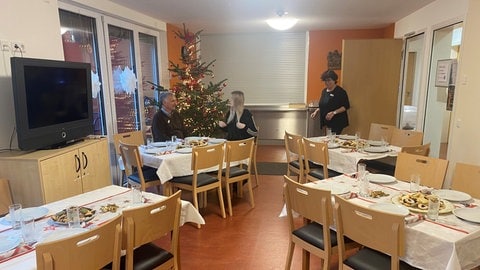 Drei Beschäftigte der Caritas schmücken die Tische in der Wärmestube der Wohnungslosenhilfe in Aalen. Die Vorbereitungen für Weihnachten für Bedürftige an Heiligabend laufen. 