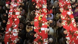 Weihnachtlich geschmückte und voll besetzte Tischreihen aus der Vogelperspektive (Symbolbild). Regen Besuch erwartet auch das evangelische Gemeindehaus in Aalen. Dort wird an Heiligabend für Obdachlose ein Festessen zubereitet. Auch in Städten wie Ulm, Schwäbisch Gmünd und Heidenheim gibt es Einladungen für Jedermann zu Weihnachten.