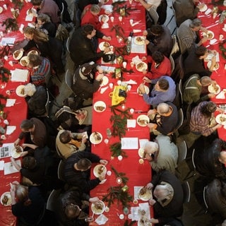 Weihnachtlich geschmückte und voll besetzte Tischreihen aus der Vogelperspektive (Symbolbild). Regen Besuch erwartet auch das evangelische Gemeindehaus in Aalen. Dort wird an Heiligabend für Obdachlose ein Festessen zubereitet. Auch in Städten wie Ulm, Schwäbisch Gmünd und Heidenheim gibt es Einladungen für Jedermann zu Weihnachten.