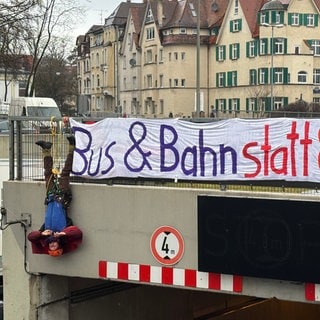 Ein Mann hängt bei einer Protestaktion am Montag kopfüber neben einem Transparent an einer Tunneeinfahrt der B10 in Ulm. Umweltaktivisten wollen mit der erneuten Aktion ihre Forderungen bekräftigen.