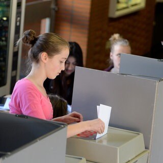 Junge Menschen stehe an einer Wahlurne an. Bei der Bundestagswahl gilt nach wie vor: Wählen ist erst ab 18 Jahren erlaubt. Forderungen, das Wahlalter zu senken, blieben bislang unerfüllt. 