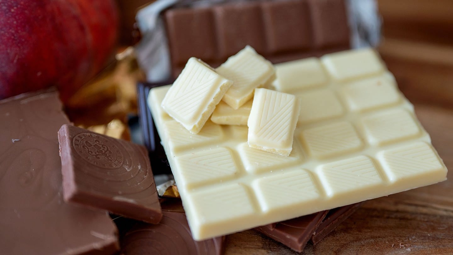 Eine angebrochene Tafel weißer Schokolade liegt neben Vollmilchschokolade