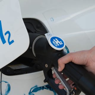 Der Tankdeckel Autos mit der Aufschrift "H2" für Wasserstoff steht offen und der Tank wird an einer Zapfsäule befüllt.
