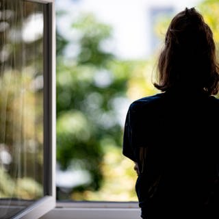 Silhouette einer Frau vor einem geöffneten Fenster.