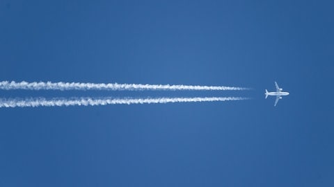 Flugzeug vor blauem Himmel mit Kondensstreifen hinter sich.