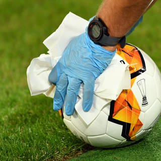 Ein Helfer mit blauen Latexhandschuhen desinfiziert einen Fußball