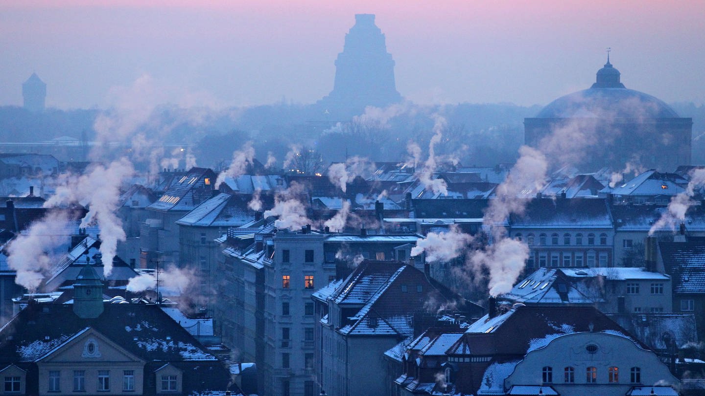Nach einer Frost-Nacht qualmen am Morgen Schornsteine von Wohnhäusern vor der Kulisse des Völkerschlachtdenkmals in Leipzig.