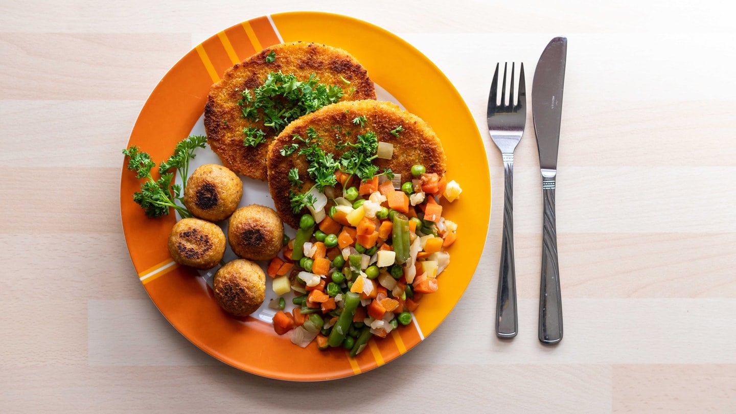 Falafel, vegane Schnitzel und Gemüse liegen garniert mit Petersilie auf einem Teller in einer Küche