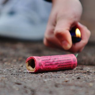 Ein Feuerzeug in der Hand eines Jugendlichen zündet einen Böller auf der Straße