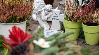 Eine Gedenkfigur und Blumen sind an der Gedenkstätte für zwei im Dienst getötete Polizisten in der Nähe des Tatorts an der K 22 bei Kusel aufgestellt.