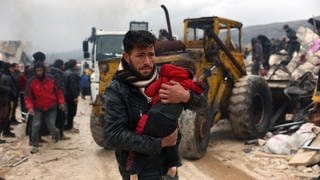 Ein Mann trägt ein Kleinkind durch Trümmer in einer türkischen Stadt.
