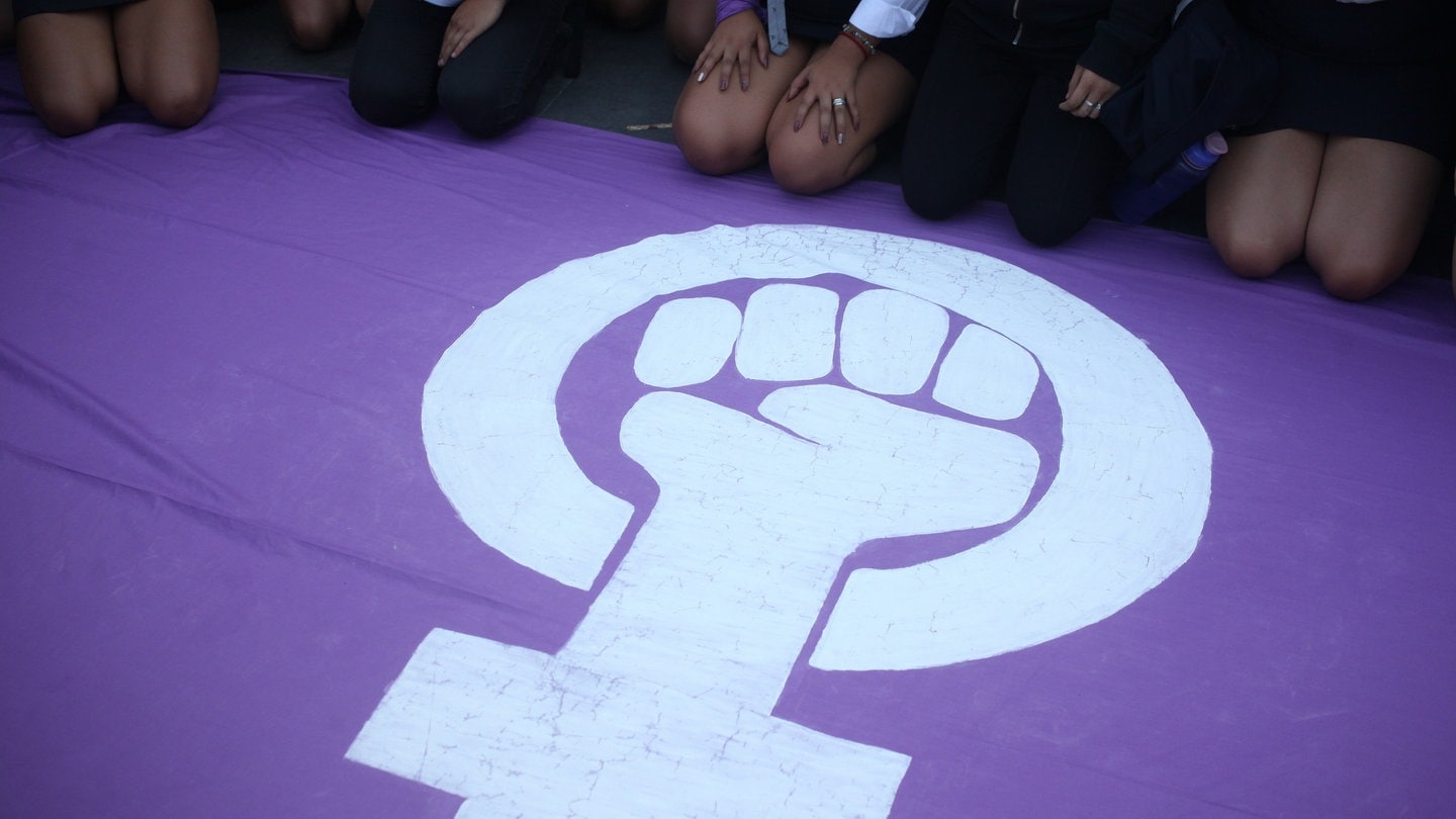 Frauen sitzen auf einer Fahne mit dem feministischen Symbol während eines Protestes.