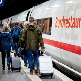 Fahrgäste gehen am frühen Morgen mit ihrem Gepäck über einen Bahnsteig am Hauptbahnhof