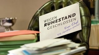 Symbolbild mit vollem Schreibtisch und Schild "Wegen Ruhestand geschlossen"