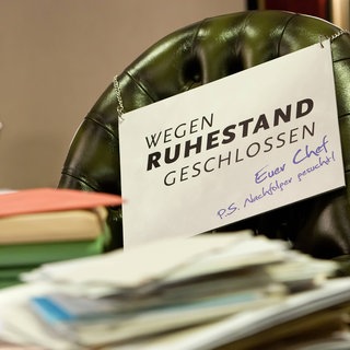 Symbolbild mit vollem Schreibtisch und Schild "Wegen Ruhestand geschlossen"