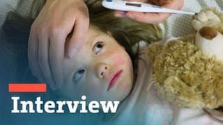Ein dreijähriges Mädchen liegt krank im Bett, die Mutter fühlt die Stirn und liest ein Fieberthermometer ab