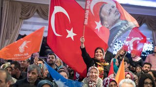 Türkische Flaggen mit dem Konterfei des türkischen Präsidenten Erdogan schwenken Anhängerinnen während einer Wahl-Veranstaltung eines türkischen AKP-Abgeordneten in einer privaten Veranstaltungshalle im hessischen Kelsterbach.