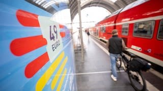 Ein Mann geht mit seinem Fahrrad an einer Deutschlandticket-Werbung und einem Regionalzug vorbei