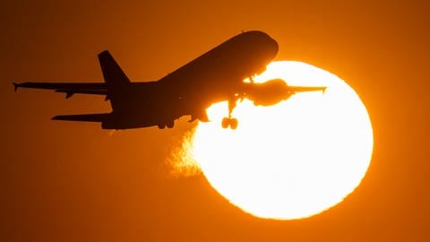 Eine Passagiermaschine hebt vor der untergehenden Sonne vom Flughafen Frankfurt ab.