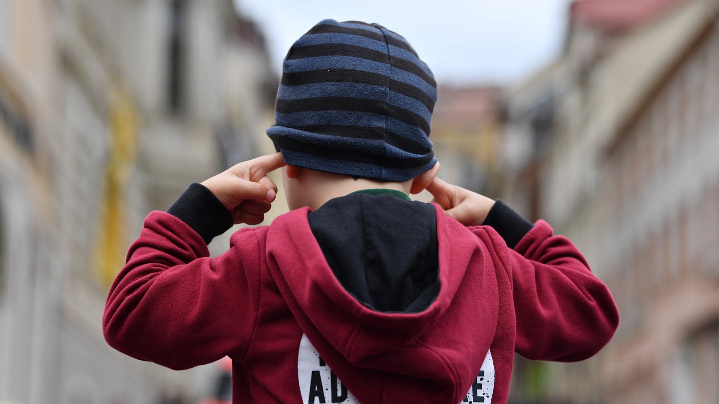 Ein etwa dreijähriger Junge steckt sich die Finger in die Ohren, um sich vor Lärm zu schützen
