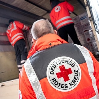 Mitarbeiter des Deutschen Roten Kreuzes verladen an einer Halle Hilfsgüter in einem LKW für den Auslandseinsatz.